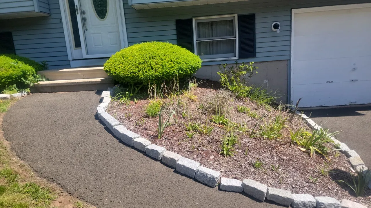 Curved driveway-side planting bed with mixed shrubs and stone edging on a manicured green lawn