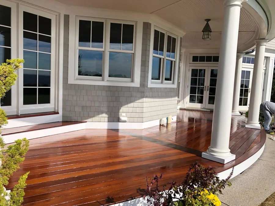 Freshly refinished curved wood deck with white columns on a gray shingle-style Connecticut home