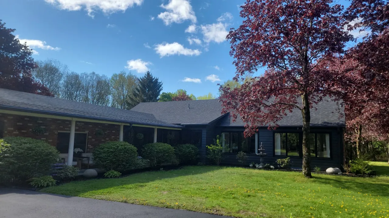 Manicured front lawn with a red Japanese maple, trimmed foundation shrubs, and a paver walkway in front of a white Connecticut home