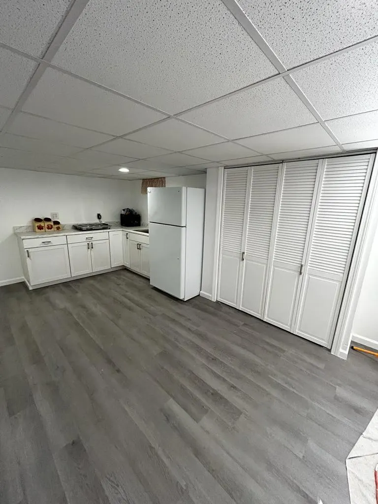 Basement room with newly installed gray vinyl plank flooring and white cabinetry